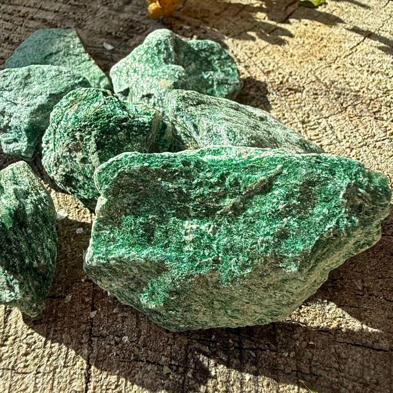Flere små rå Fuchit natursten med grønne glitrende overflader på træ